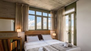 Hotelkamer met een groot bed, twee nachtkastjes met lampen, uitzicht op de bergen door de ramen en een openslaande deur naar het balkon.