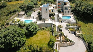 Een moderne villa met een zwembad, omringd door weelderige begroeiing en glooiend landschap.