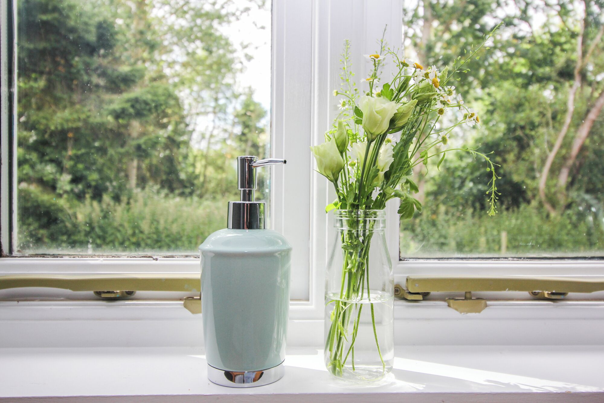 A bottle and a vase with flowers on a windowsill.