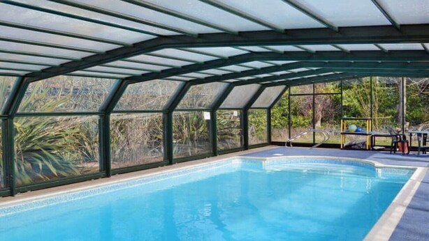 Una piscina interior con techo de cristal, rodeada de vegetación.