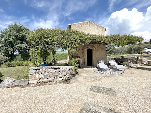 A stone structure with a doorway, surrounded by a gravel patio and outdoor seating. - House with pool in the Luberon for 6 people (Saint-Saturnin-lès-Apt)