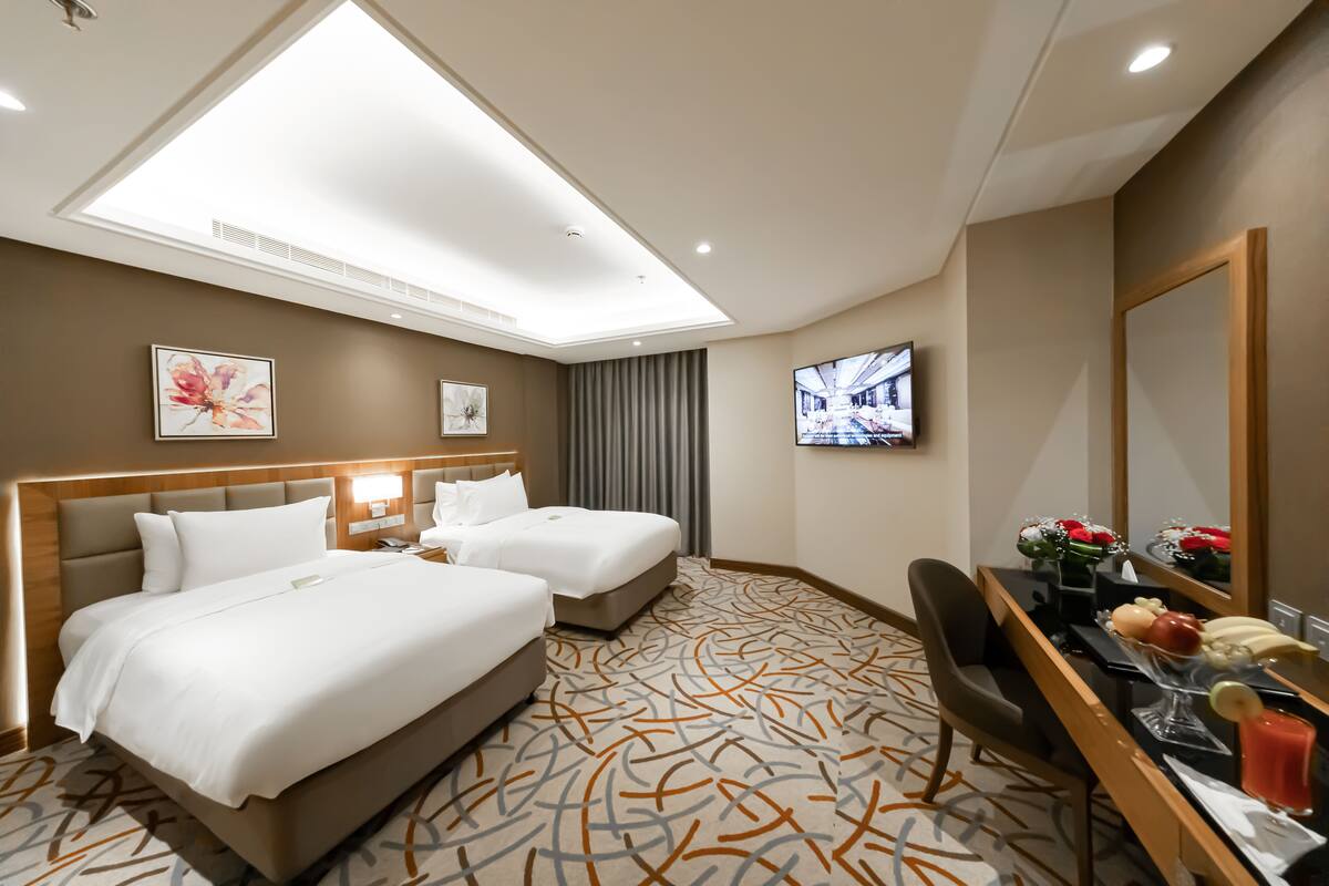 A hotel room with two beds, a desk with a mirror, a TV, and a desk lamp.