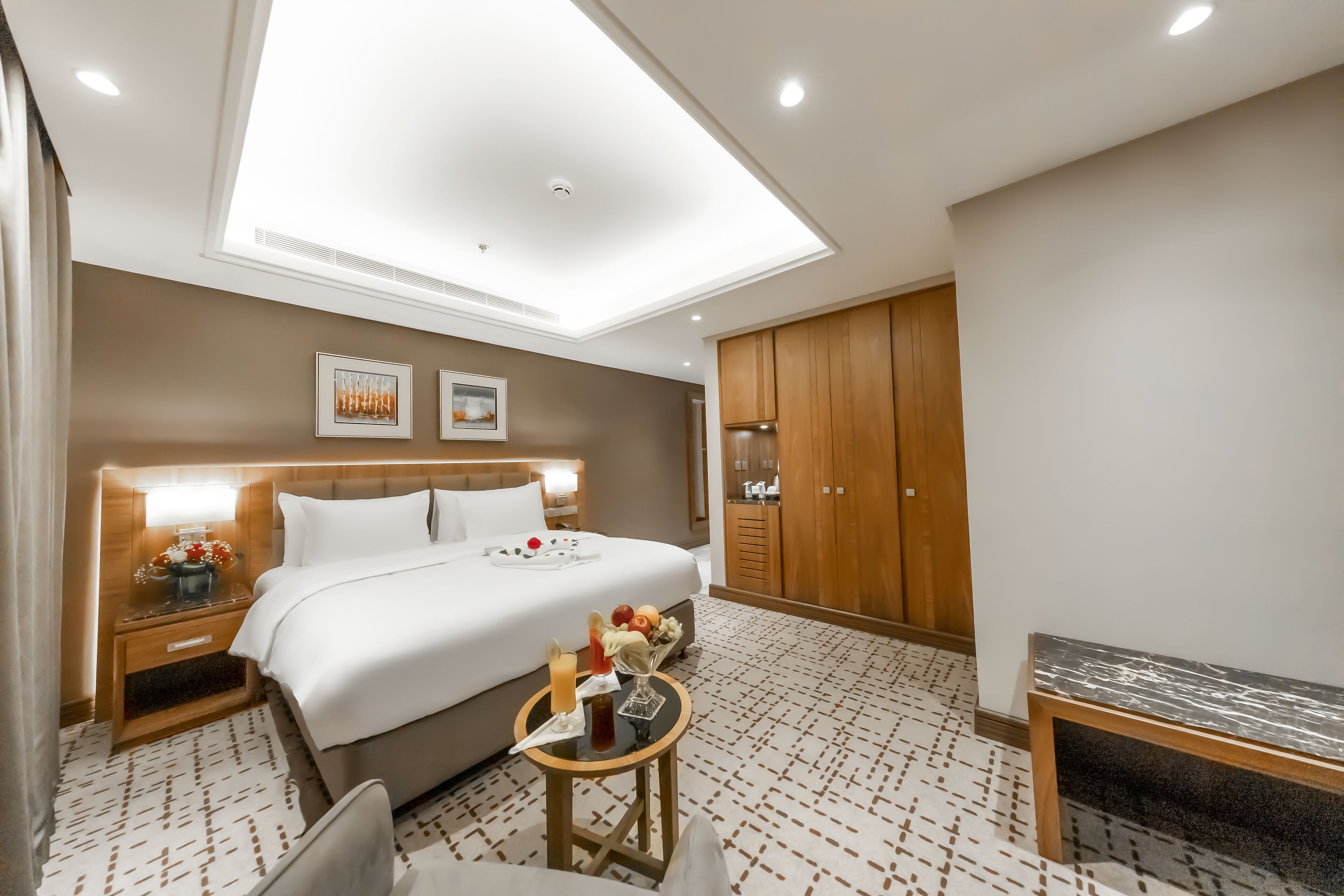 A hotel room with a large bed, a bedside table with a lamp, a small table with a vase, and a wardrobe.