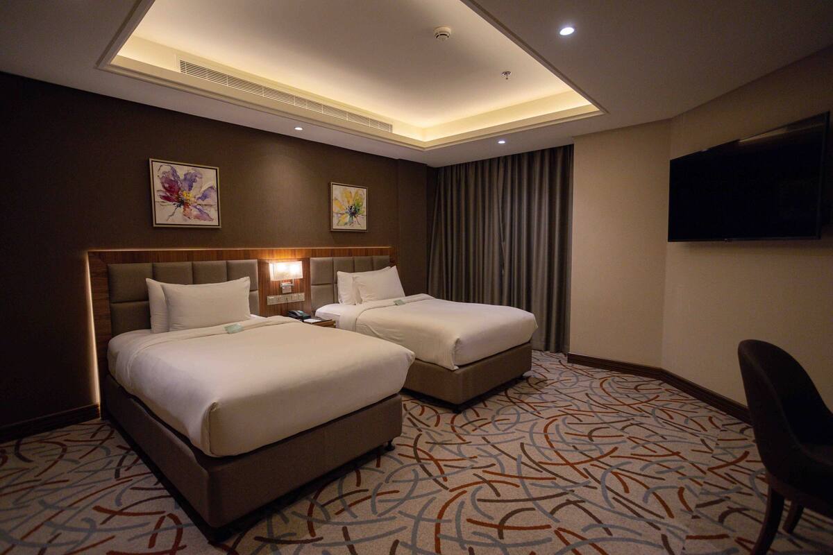 A hotel room with two beds, a flat-screen TV, and a patterned carpet.