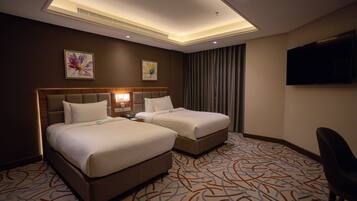 A hotel room with two beds, a flat-screen TV, and a patterned carpet.
