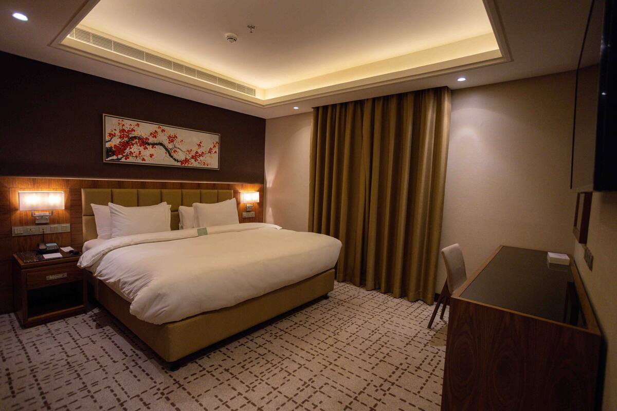 A hotel room with a large bed, bedside lamps, a desk, and a painting on the wall.
