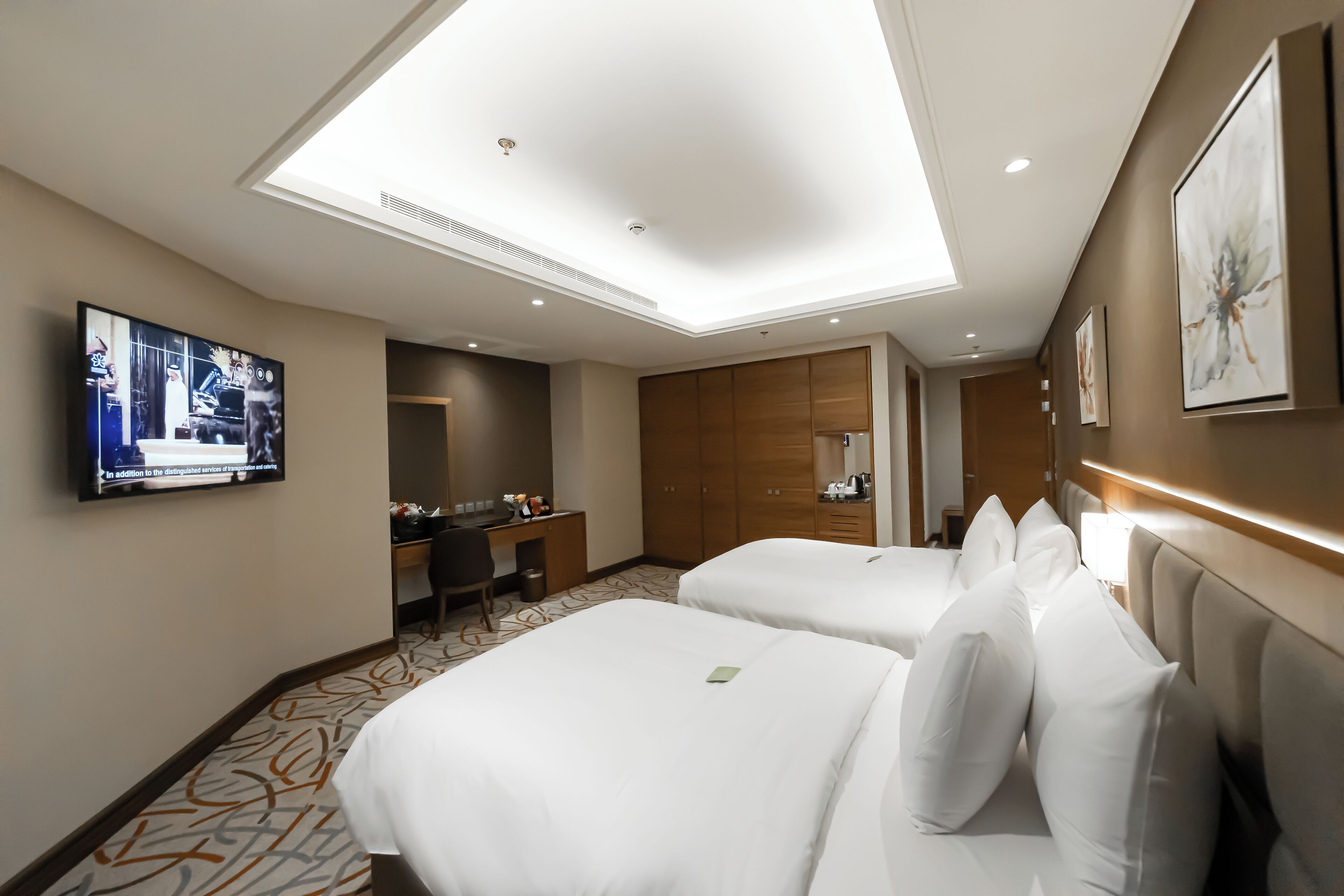 Ein Hotelzimmer mit zwei Betten, einem Schreibtisch, einem Fernseher und einer Deckenleuchte.