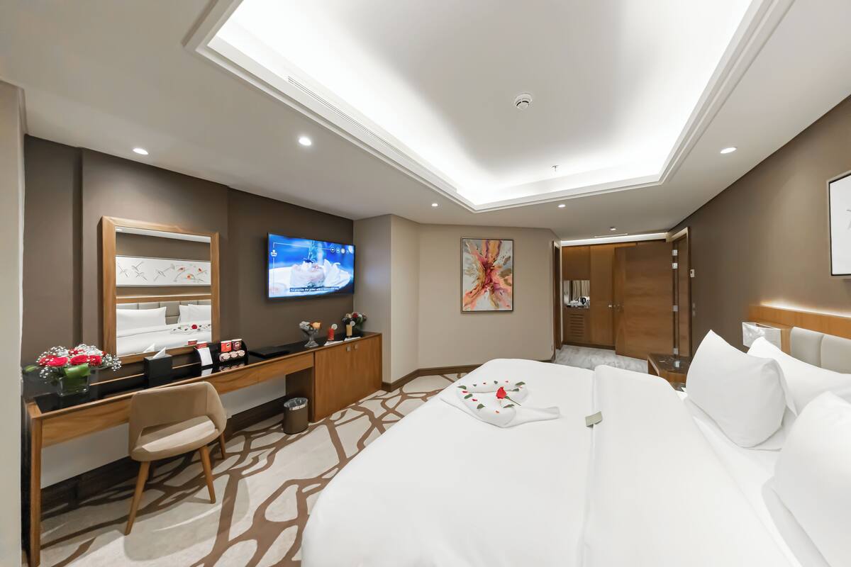 A modern hotel room with a large bed, a desk with a chair, a television, and a bathroom visible through an open door.