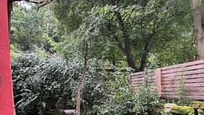 Un espacio de estar al aire libre de estilo rústico con una mesa y banca de madera, rodeado de abundante vegetación y un muro de piedra.