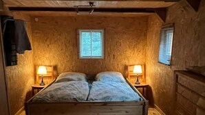 Una habitación de madera con una cama, dos mesitas de noche y dos ventanas.