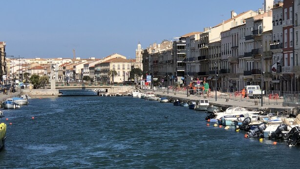 Une vue urbaine sur le front de mer, avec des bâtiments, un port de plaisance et des bateaux.