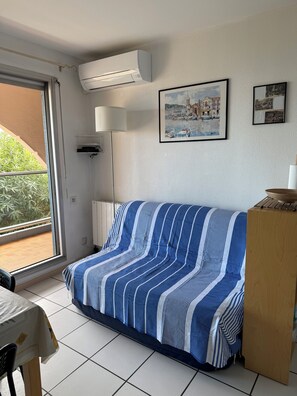 A room with a sofa covered in striped fabric, a table with a white tablecloth, a lamp, and a wooden cabinet.