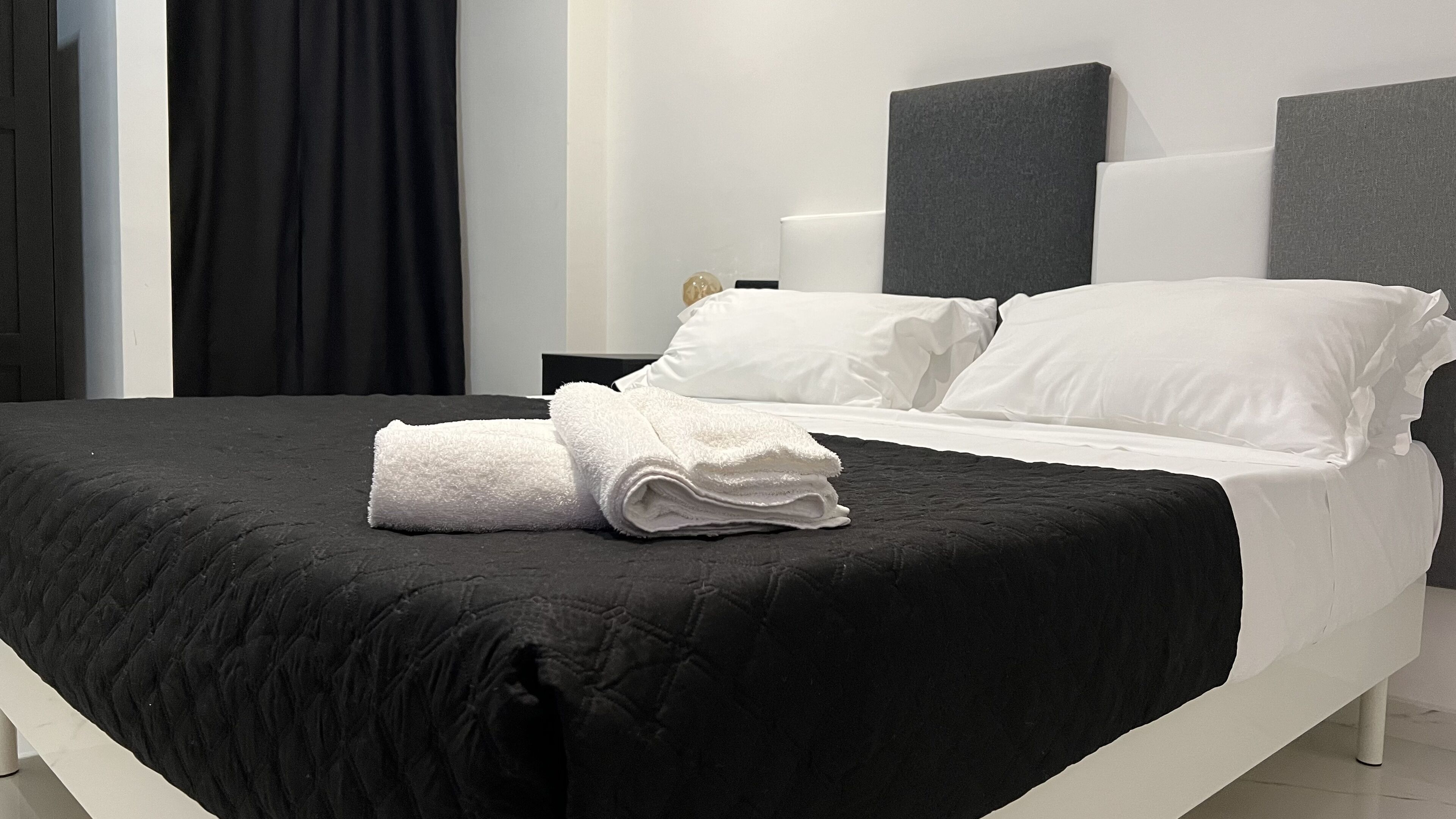 A neatly made bed with white pillows and a folded white towel on a black bedspread.