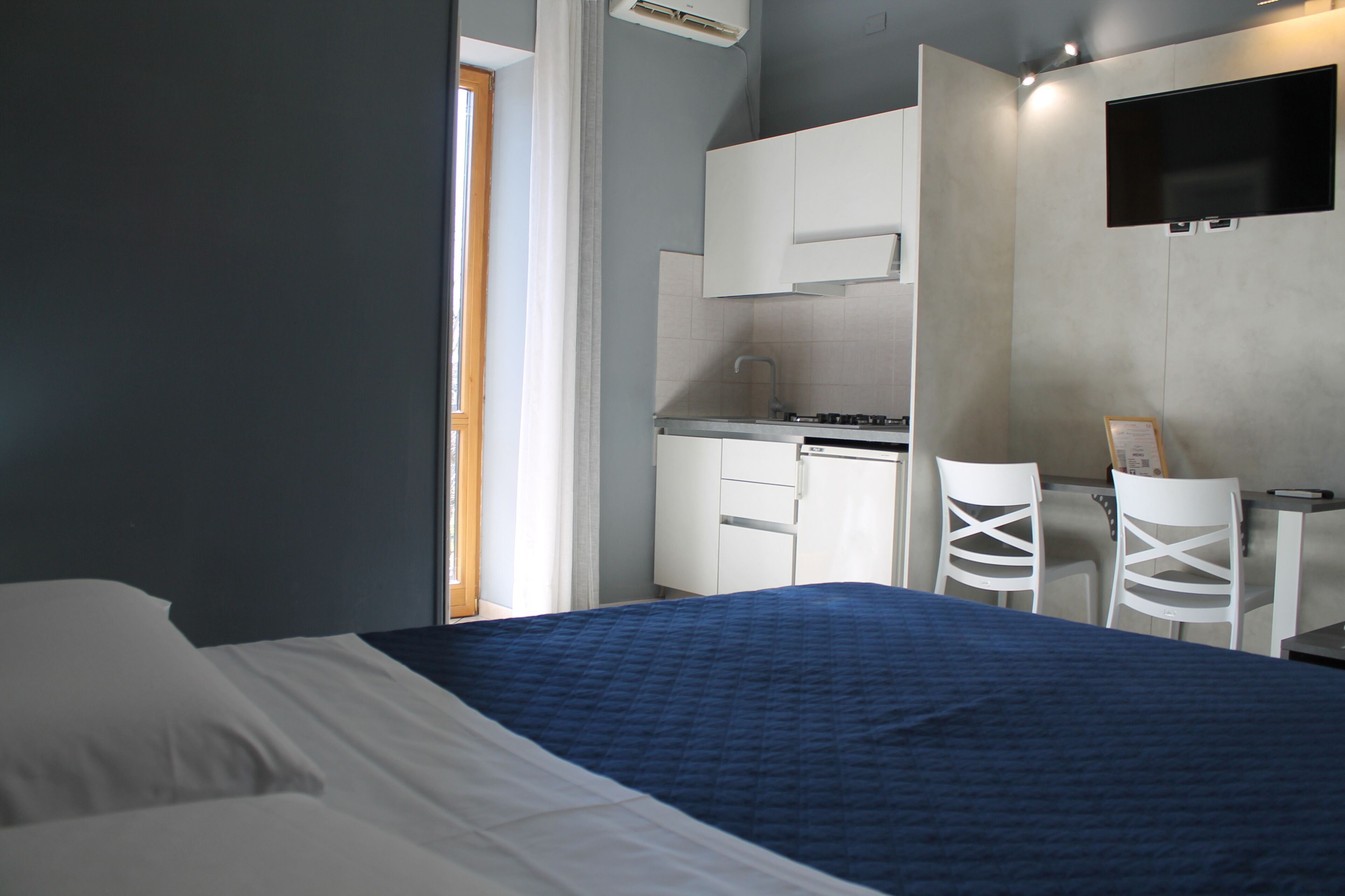 A bedroom with a bed, a desk, and a kitchenette.
