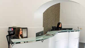 Um balcão de recepção com design curvo, tampo de vidro e um painel de parede trabalhado ao fundo.