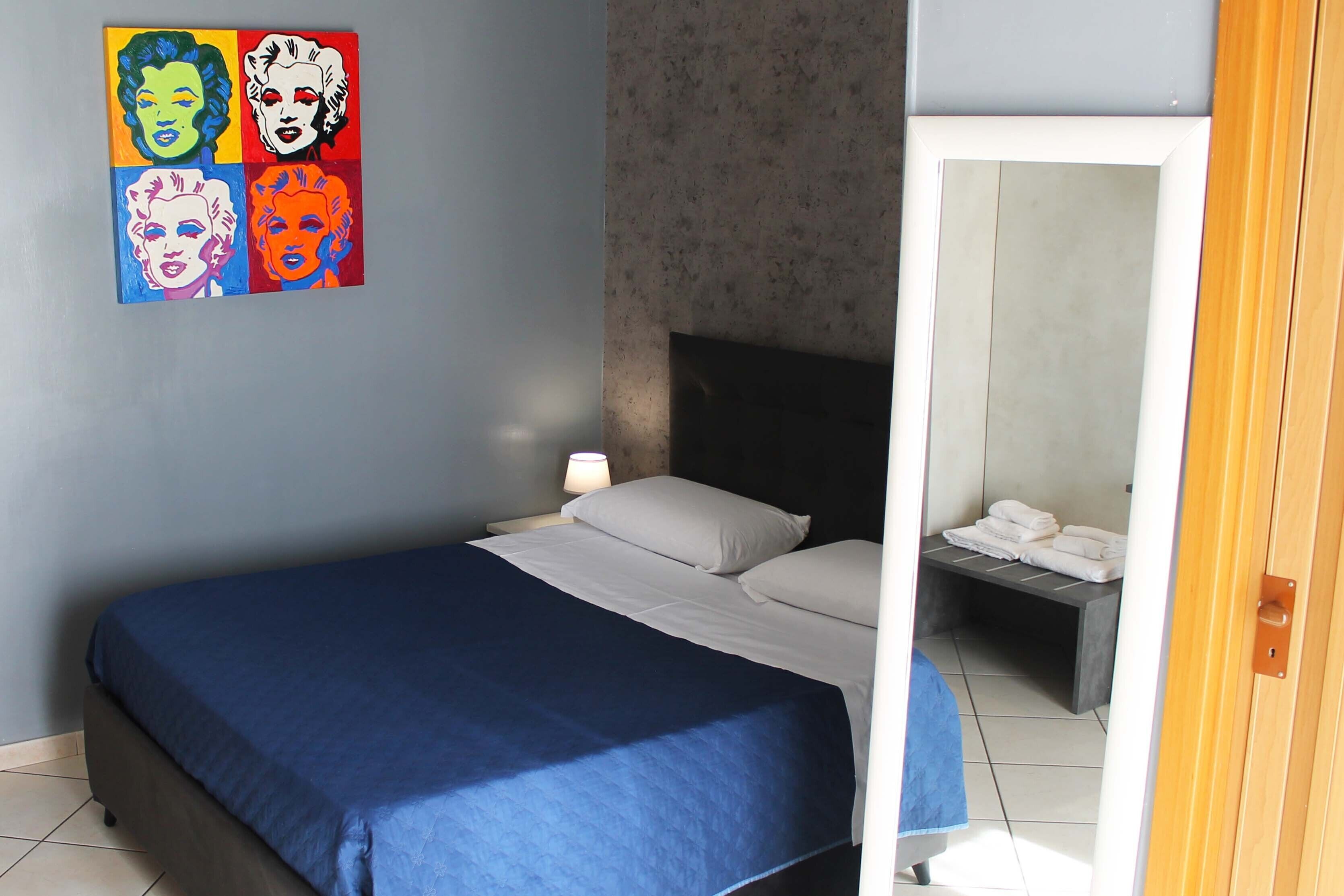 A bedroom with a bed, a nightstand, a lamp, and a painting on the wall.