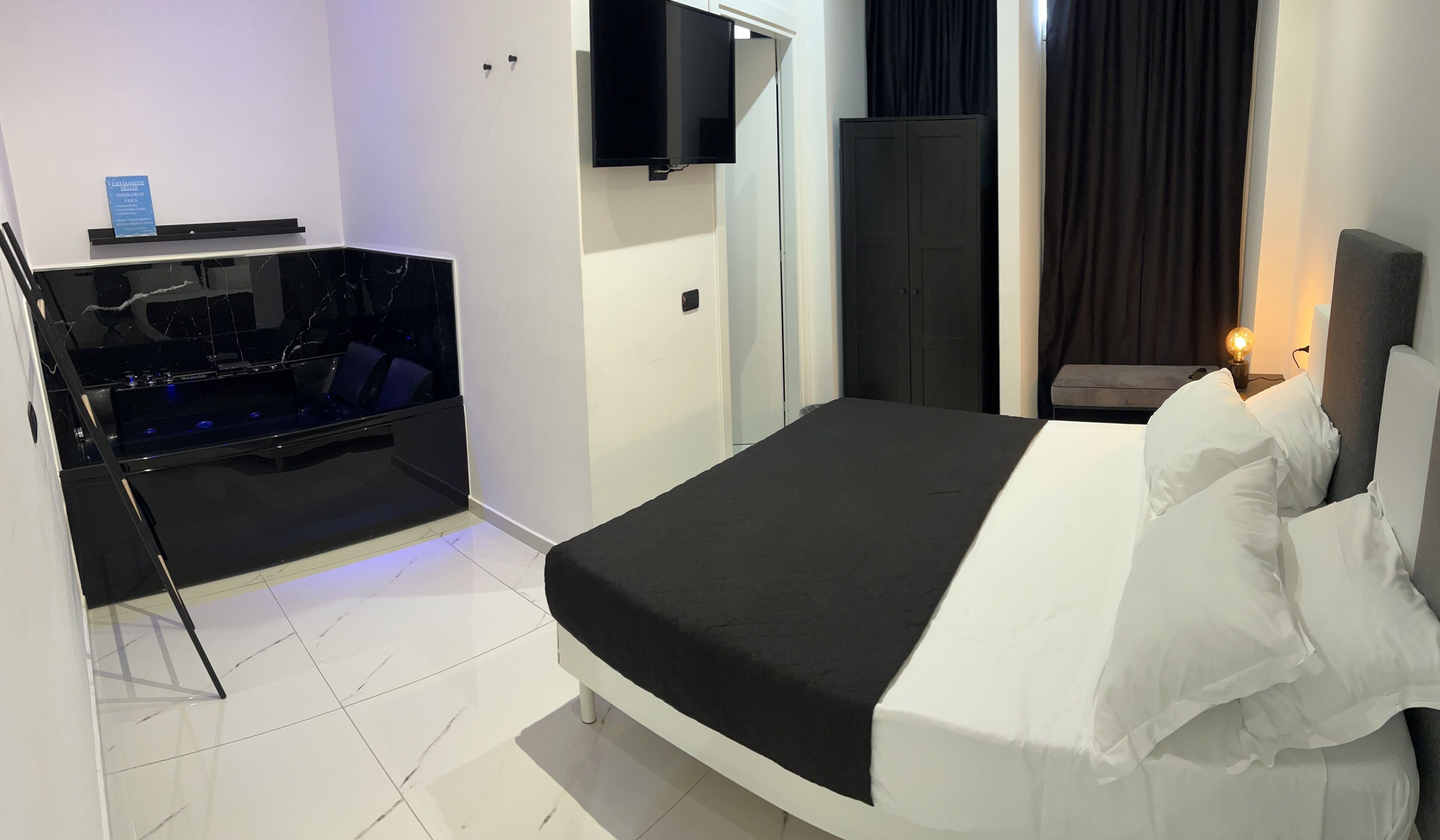 A modern hotel room with a bed, a small seating area, a flat-screen TV, and a desk with a computer.