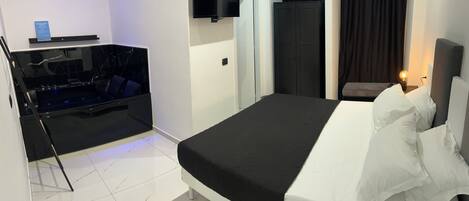 A modern hotel room with a bed, a small seating area, a flat-screen TV, and a desk with a computer.