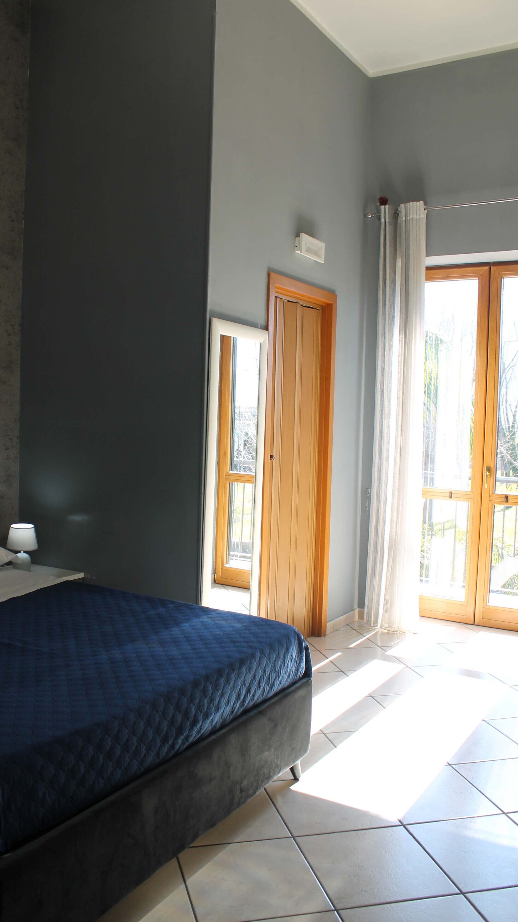 Een slaapkamer met een bed, een raam, een deur en een lichtschakelaar aan de muur.