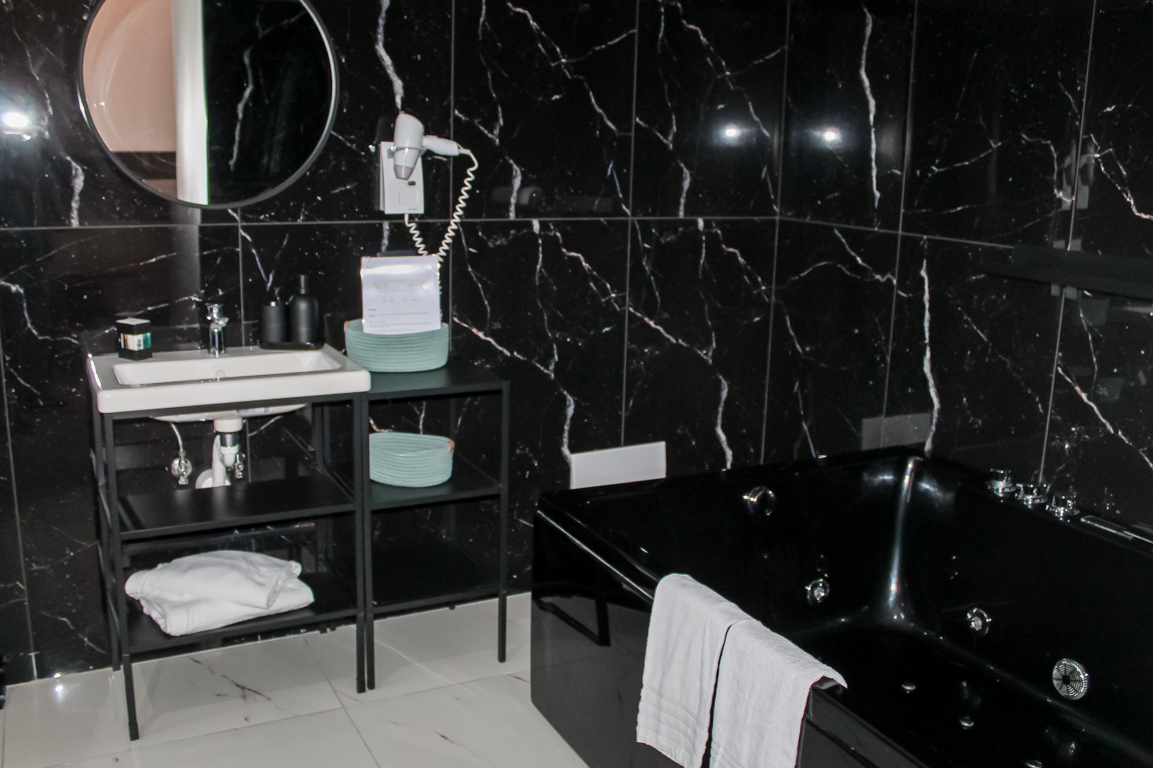 A modern bathroom with a black marble wall, a black bathtub, a white sink, and a mirror above the sink.