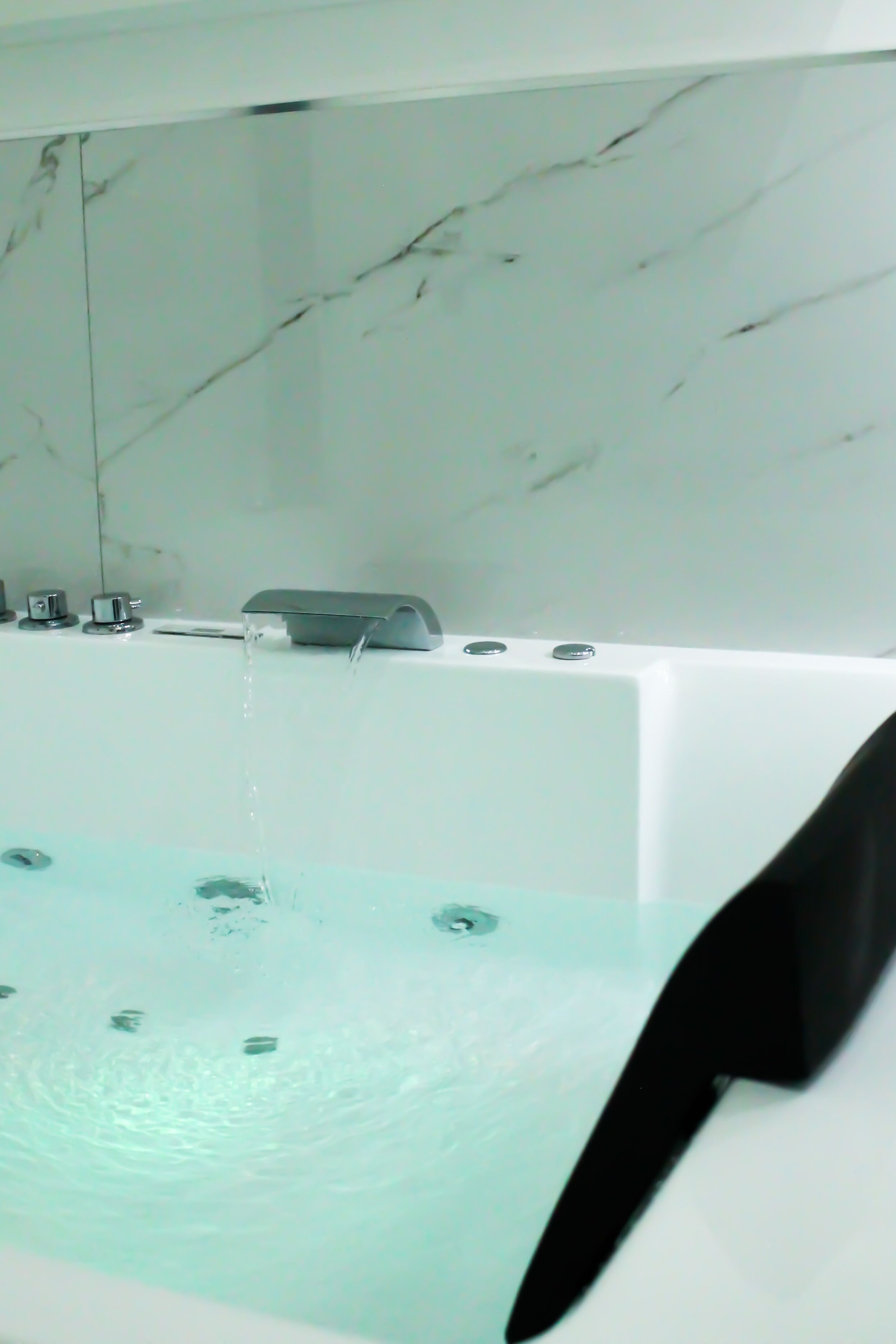 A modern bathroom with a marble wall, a bathtub with a faucet, and a showerhead.