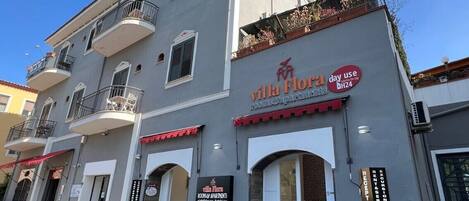 A building with a sign for 'Villa Flora' indicating it is a hotel. There are balconies with railings, and the entrance has a red awning.