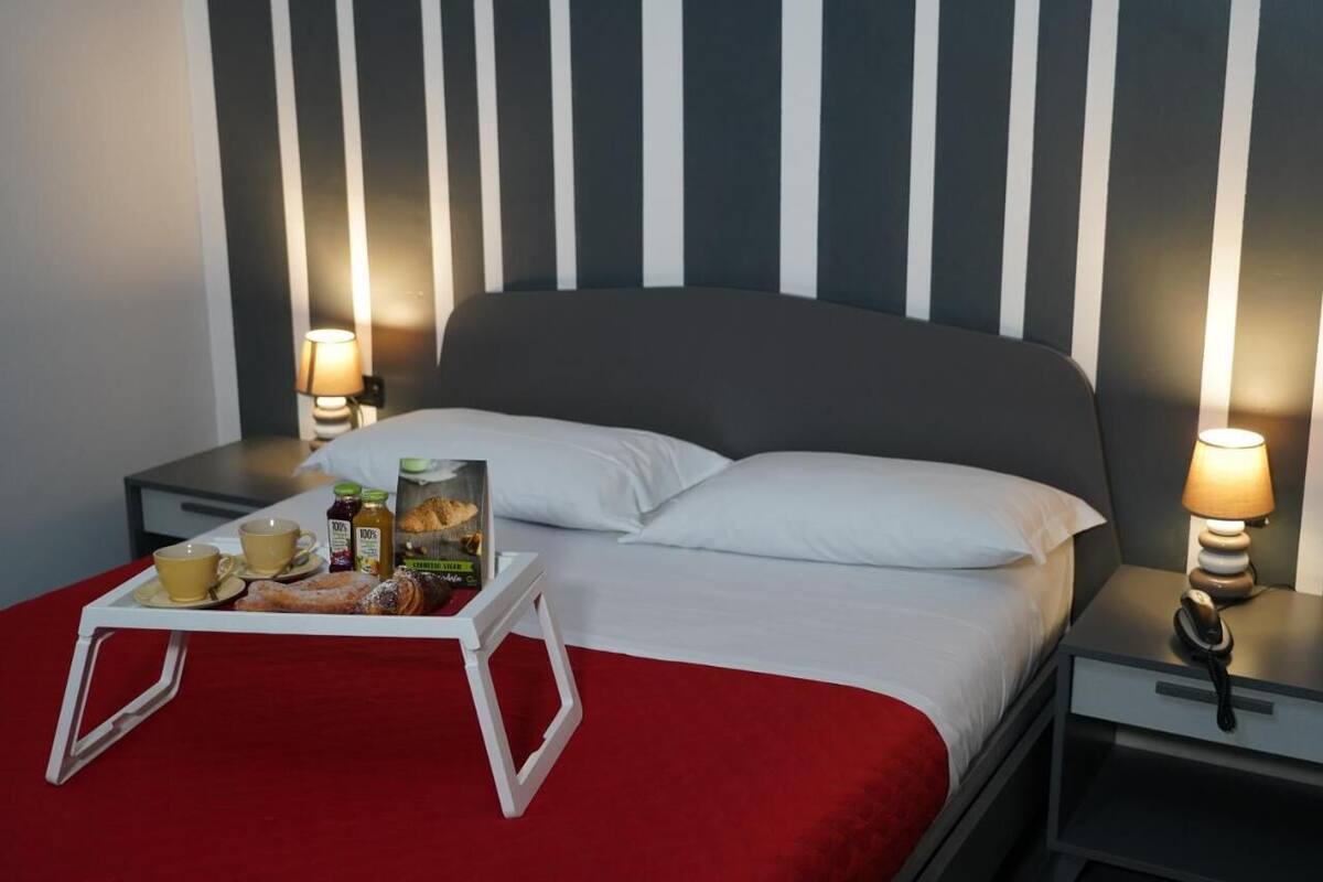 A hotel room with a bed, bedside tables, a tray with breakfast items, and lamps.