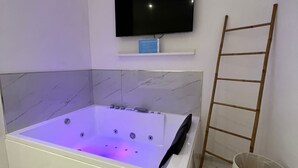 Uma casa de banho moderna com uma banheira grande, televisão fixada na parede e uma escada de madeira.