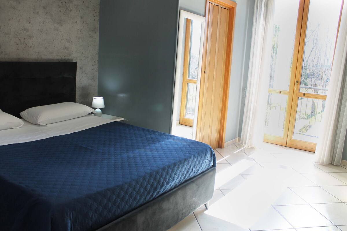 A bedroom with a bed, a nightstand, a window, and a door.