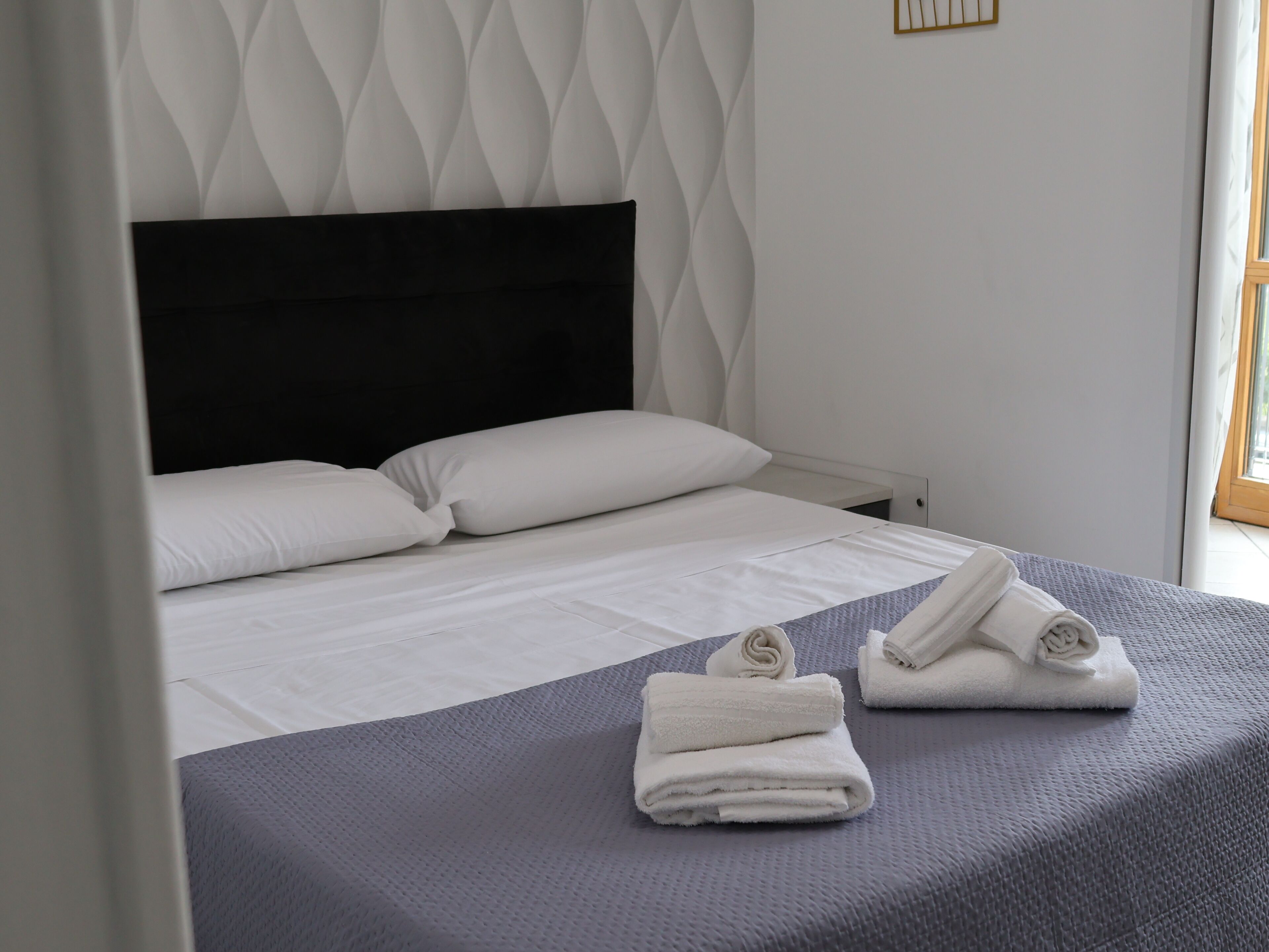 Ein Hotelzimmer mit Bett, Kissen, einem gefalteten Handtuch und einem Fenster.