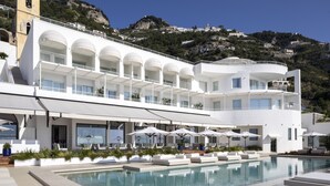 Ein modernes Hotel mit Poolbereich, Sitzgelegenheiten im Freien und Blick auf eine gebirgige Landschaft.