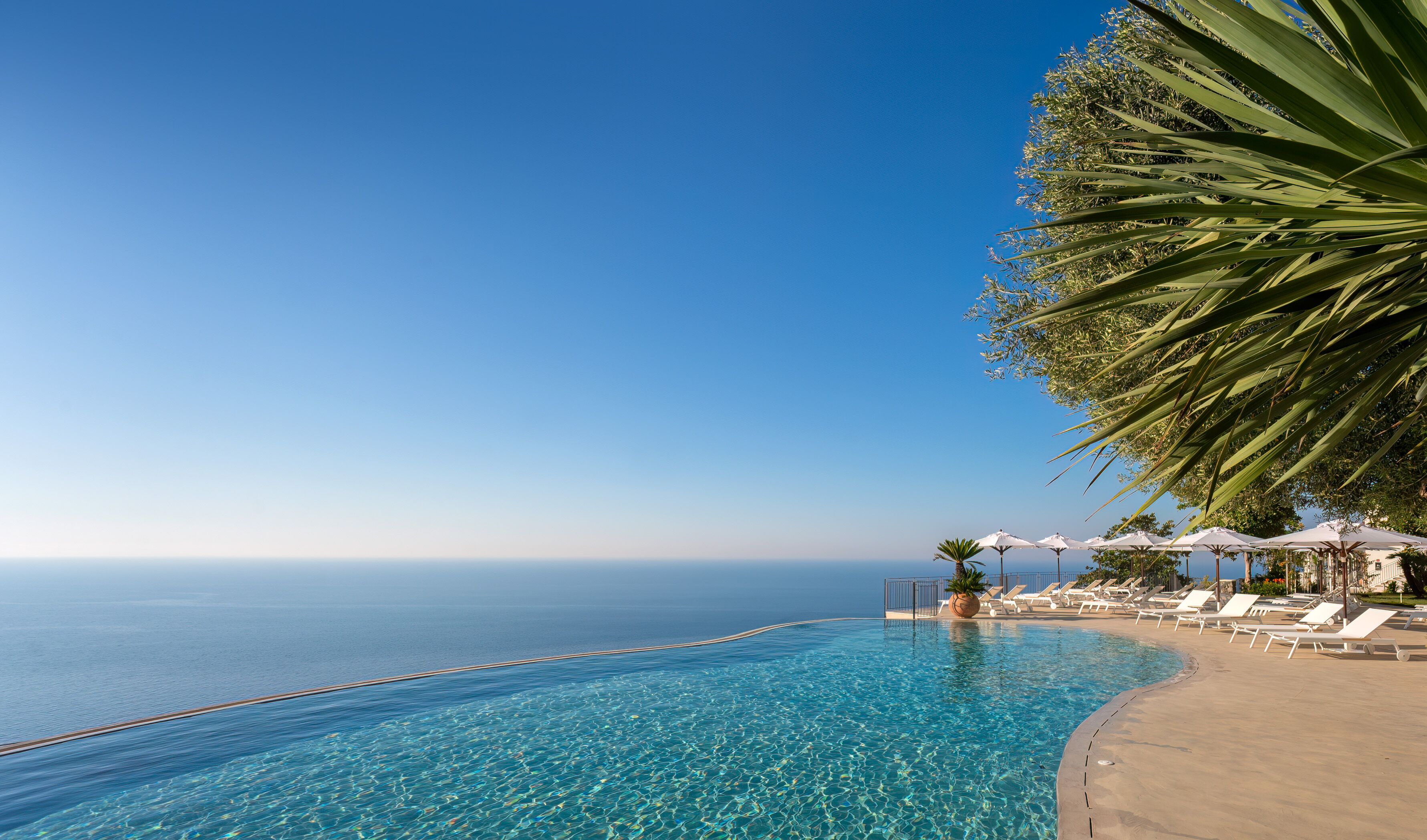 Ein strahlend blauer Himmel, ein Schwimmbad mit klarem Wasser und ein Strand mit Liegestühlen und Sonnenschirmen.