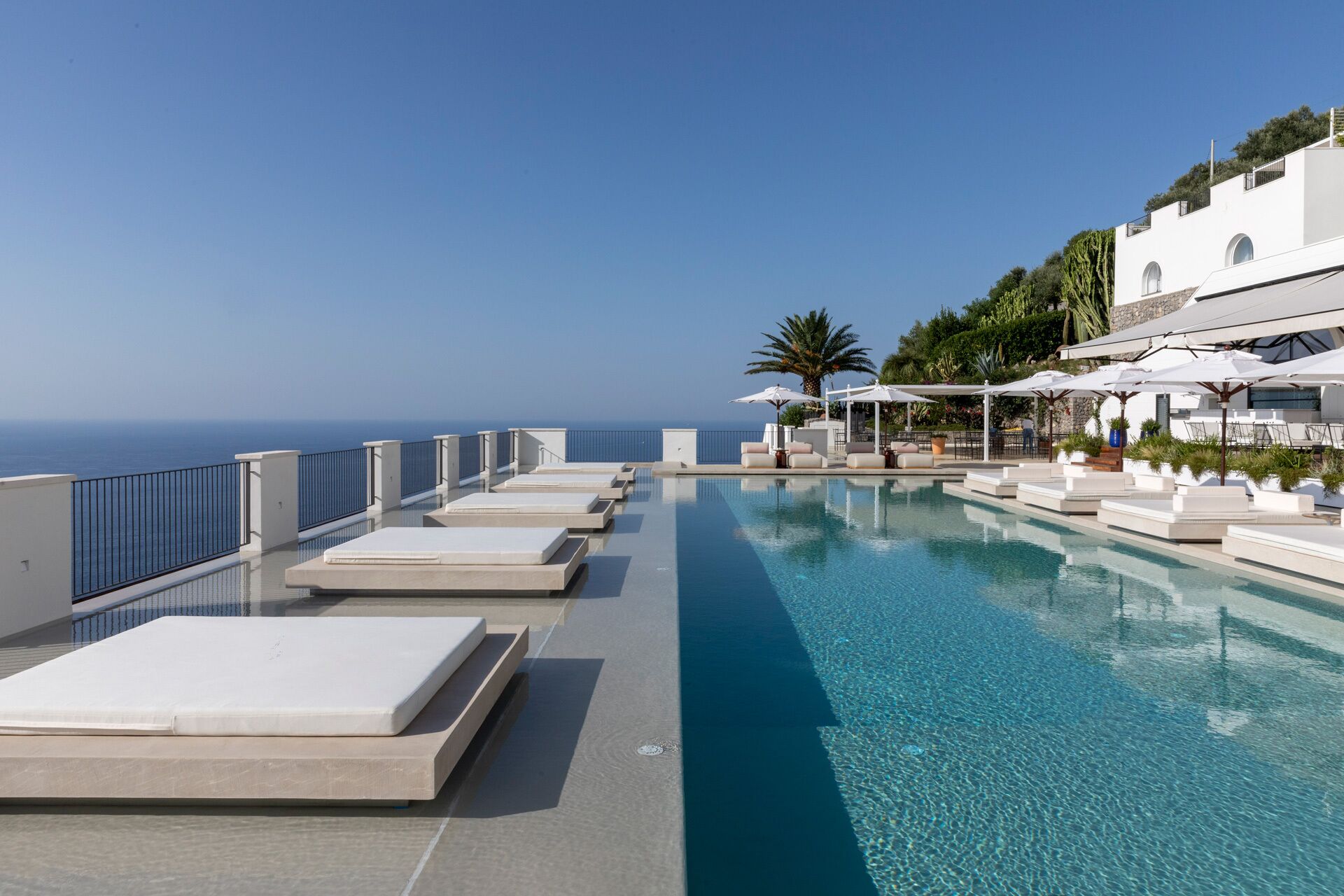 A rooftop infinity pool with lounge chairs and umbrellas, overlooking the sea.