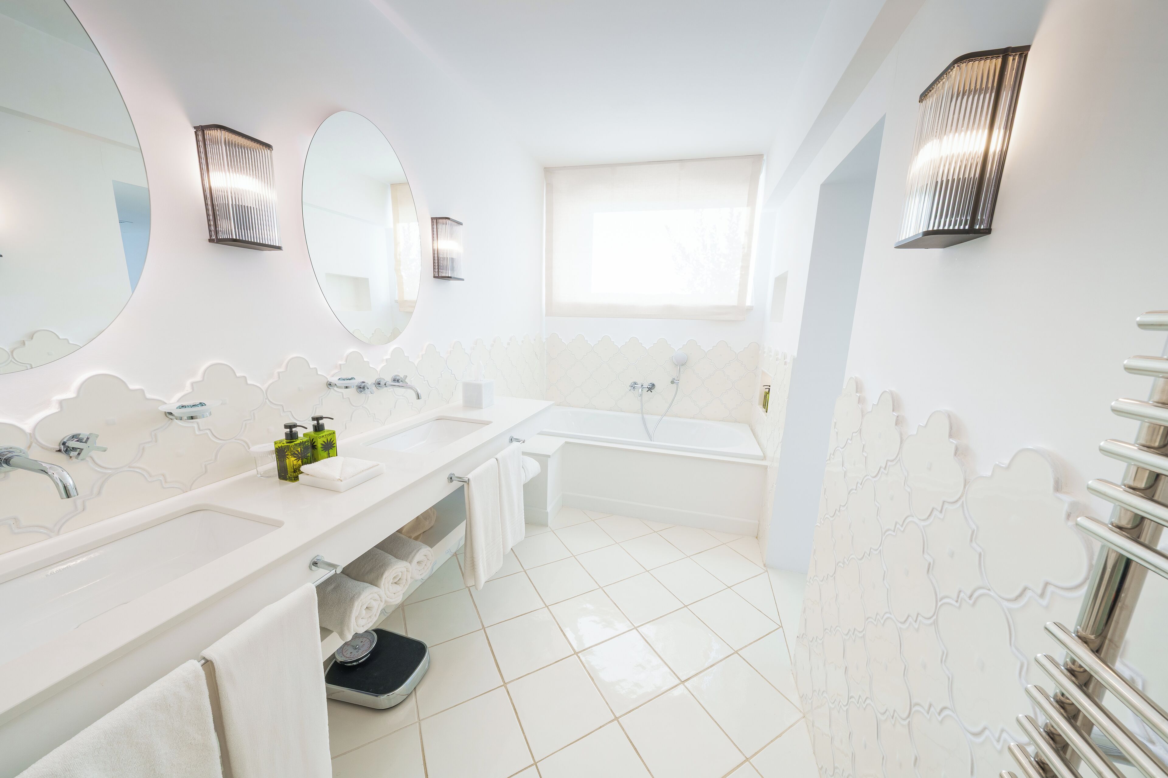 A modern bathroom with a large mirror, two sinks, a bathtub, and a towel rack.