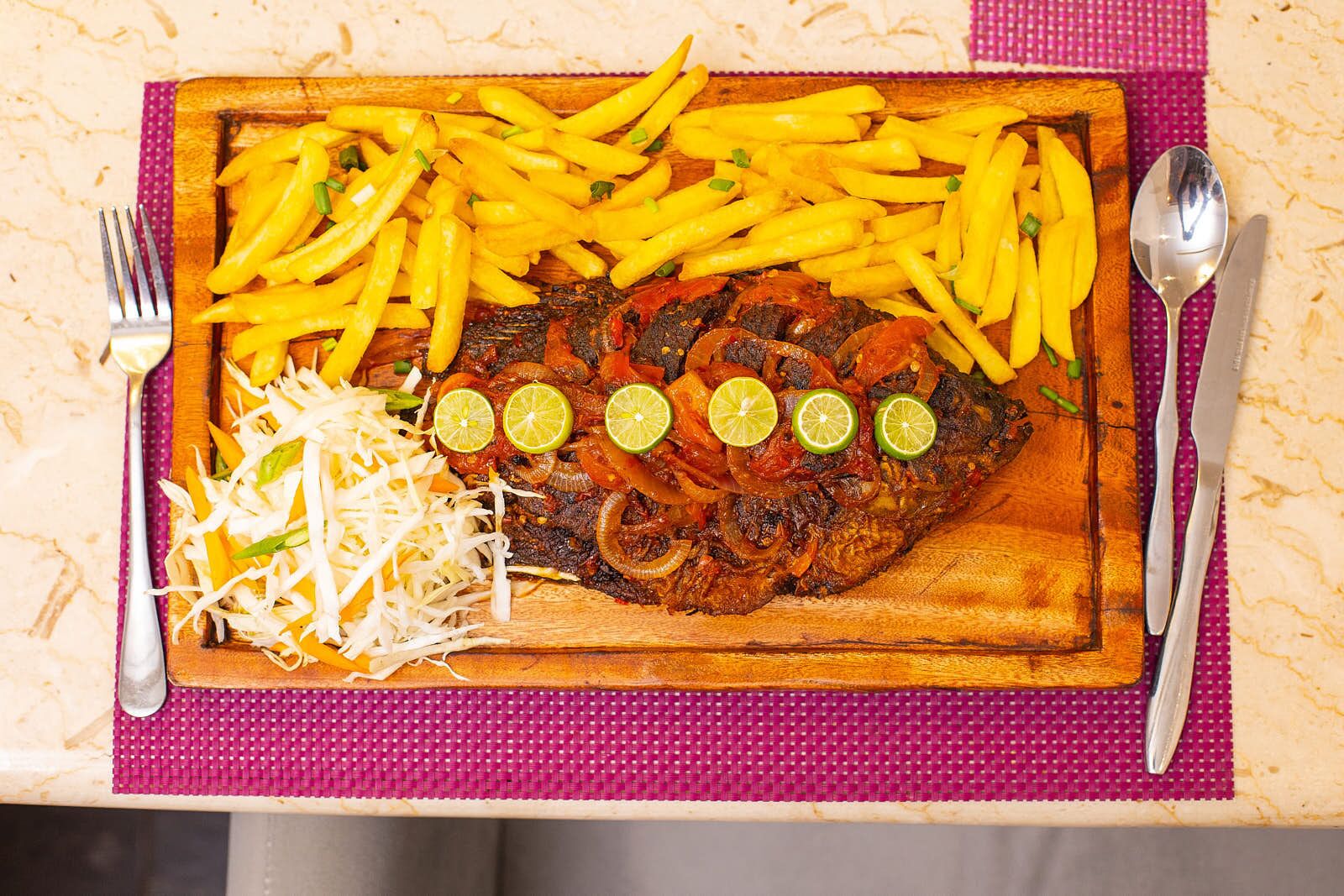 A meal with a fish dish, fries, and shredded vegetables on a wooden board.