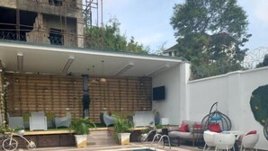 A swimming pool with a tiled deck, surrounded by outdoor seating and a building with a brick facade. - Prosbel Hotel (Abuja)