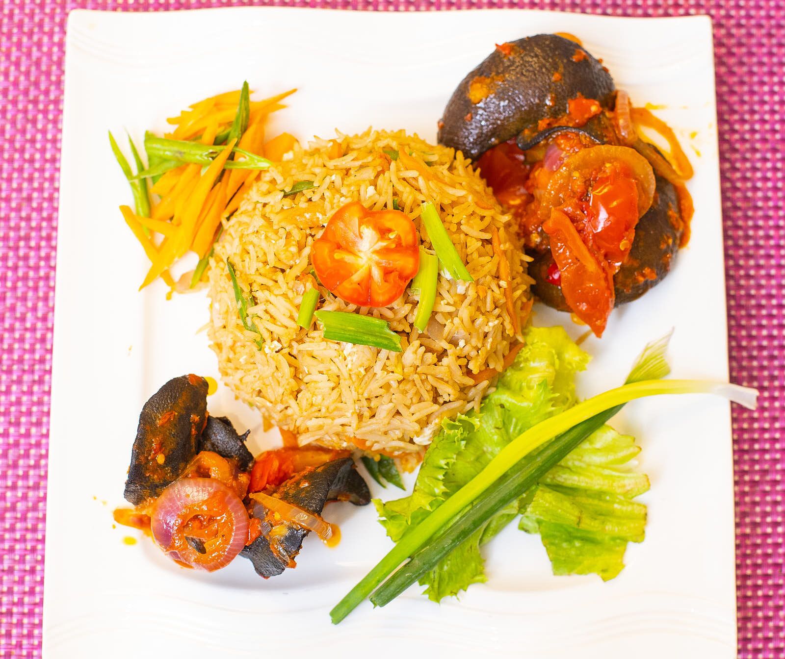 A plate of food with rice, vegetables, and a tomato slice.