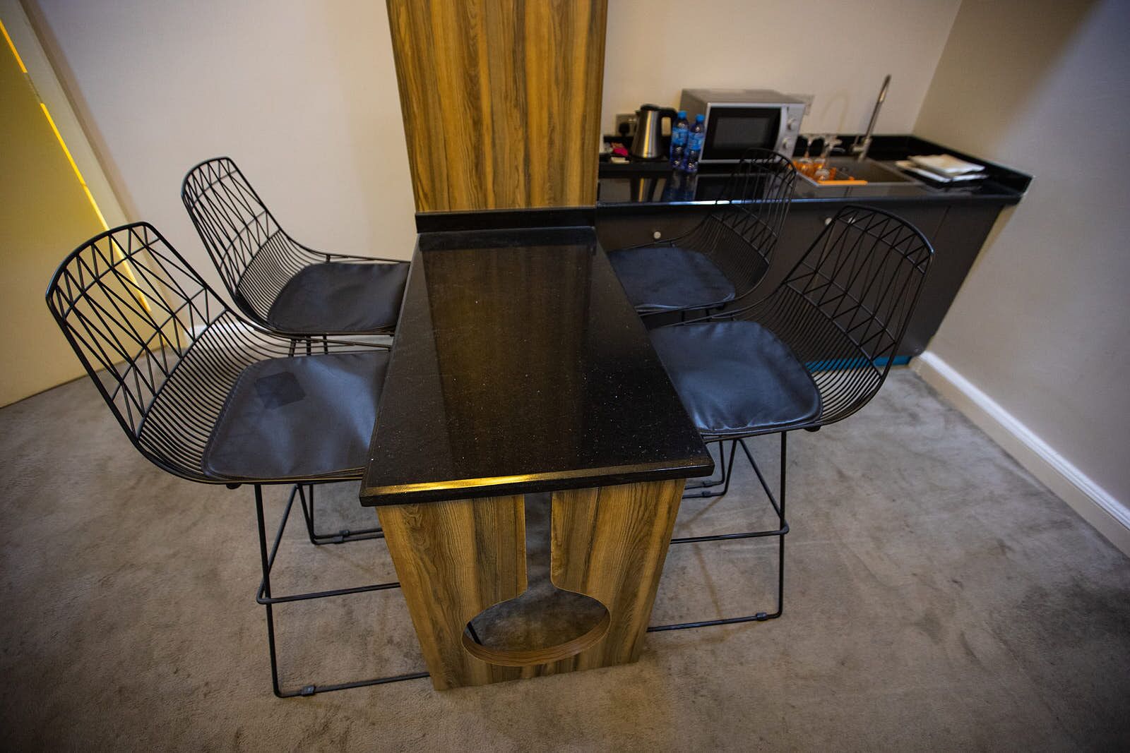 A dining table with six chairs, a wooden accent, and a small kitchen area with appliances and water bottles.