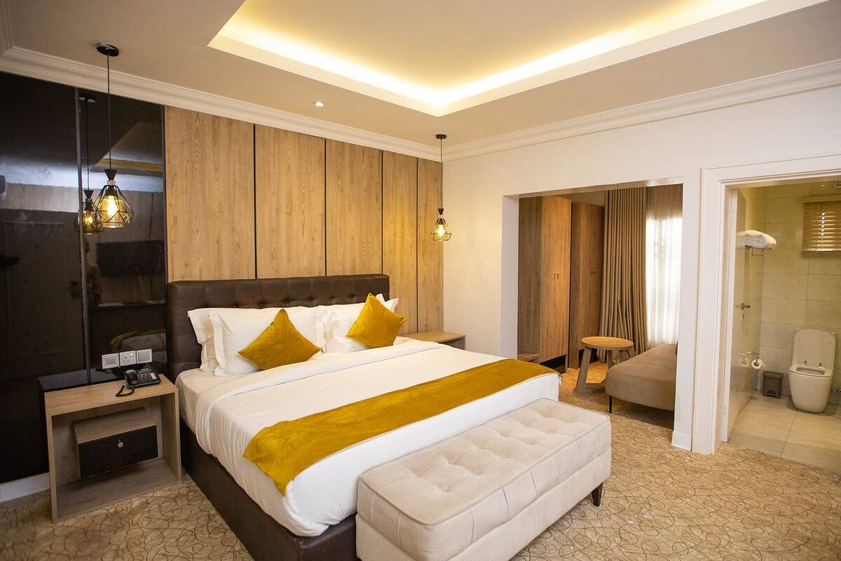 A modern hotel room with a large bed, a bedside table, a small desk, a chair, and a bathroom visible through an open door.