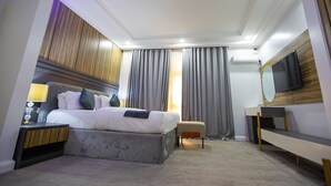 A modern hotel room with a bed, bedside table, lamp, and a TV. - Prosbel Hotel (Abuja)