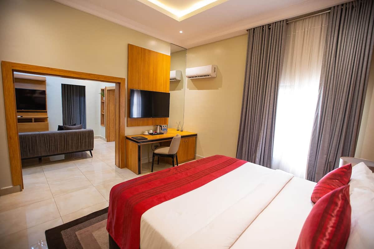 A hotel room with a bed, a desk, a chair, a television, and an air conditioning unit.