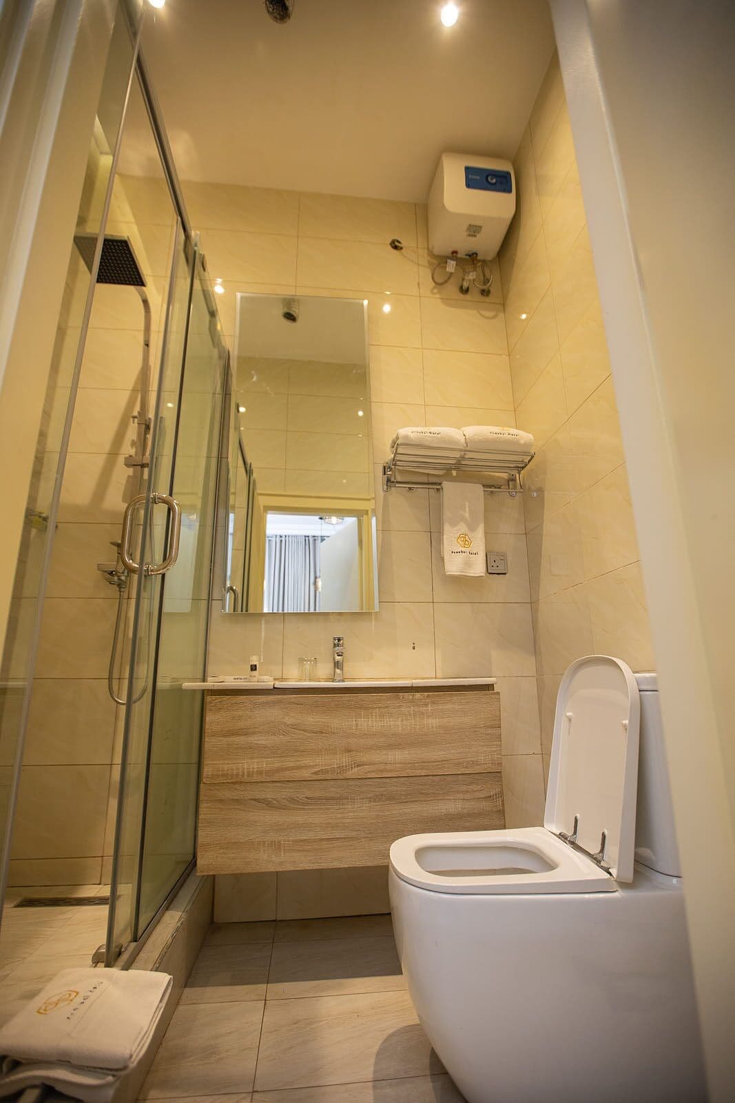 Een moderne badkamer met een glazen douchecabine, een houten wastafelmeubel, een toilet en een handdoekhouder.