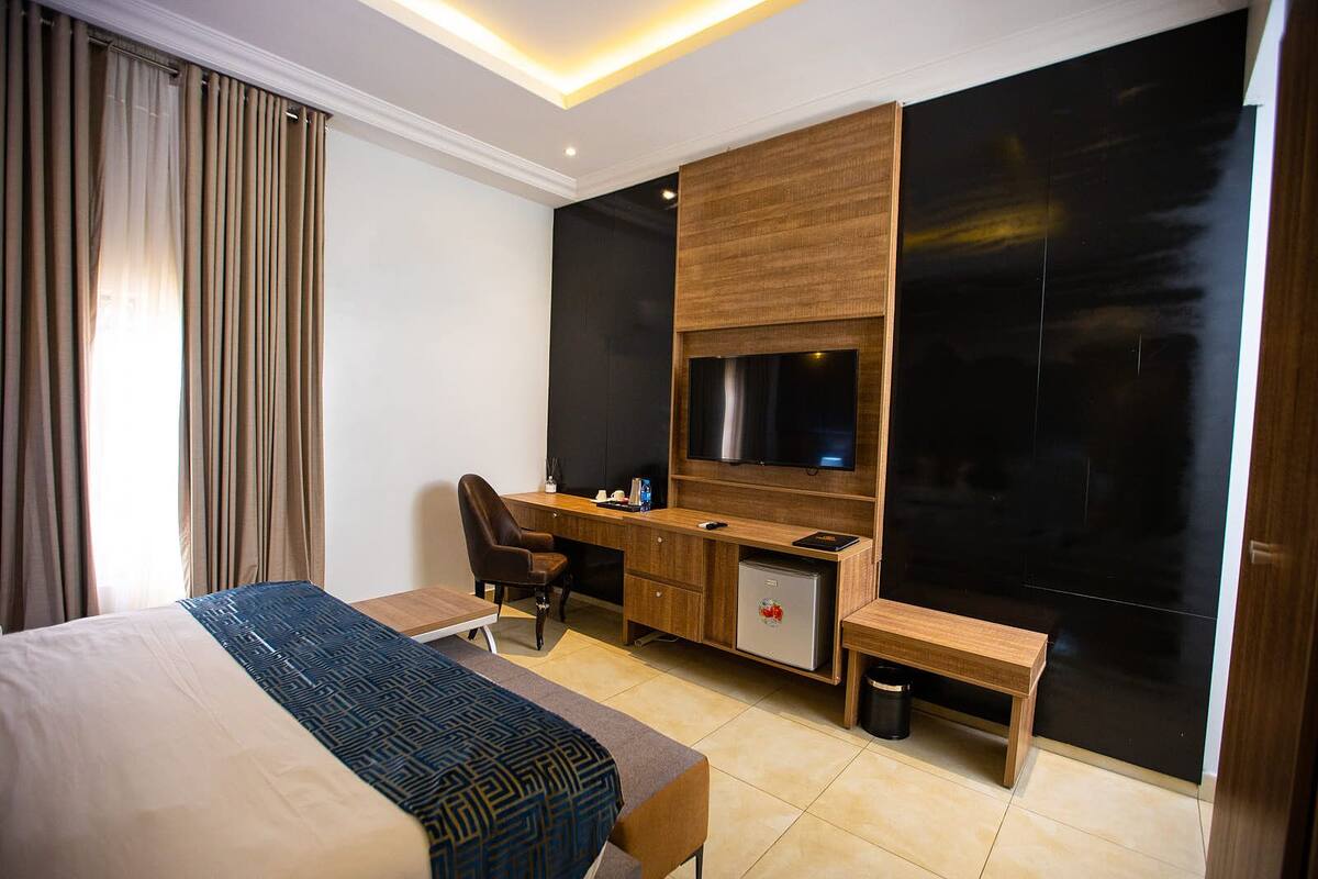 A hotel room with a bed, a desk, a chair, a TV, and a minibar.