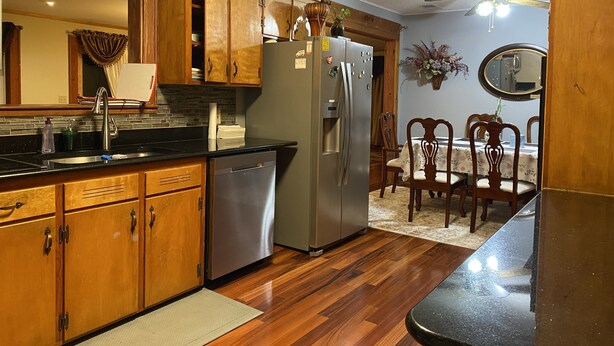 A kitchen with wooden cabinets, a stainless steel refrigerator, a dishwasher, and a dining area with a table and chairs.