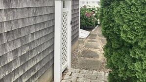 A house with grey siding, a white fence, and a stone pathway leading to a white arched gate. -  Charming Cape Cod home, minutes to Nantucket Sound (Harwich)