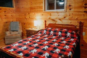 Une pièce de cabane en bois comprenant un lit, une chaise, une table de chevet et une fenêtre.