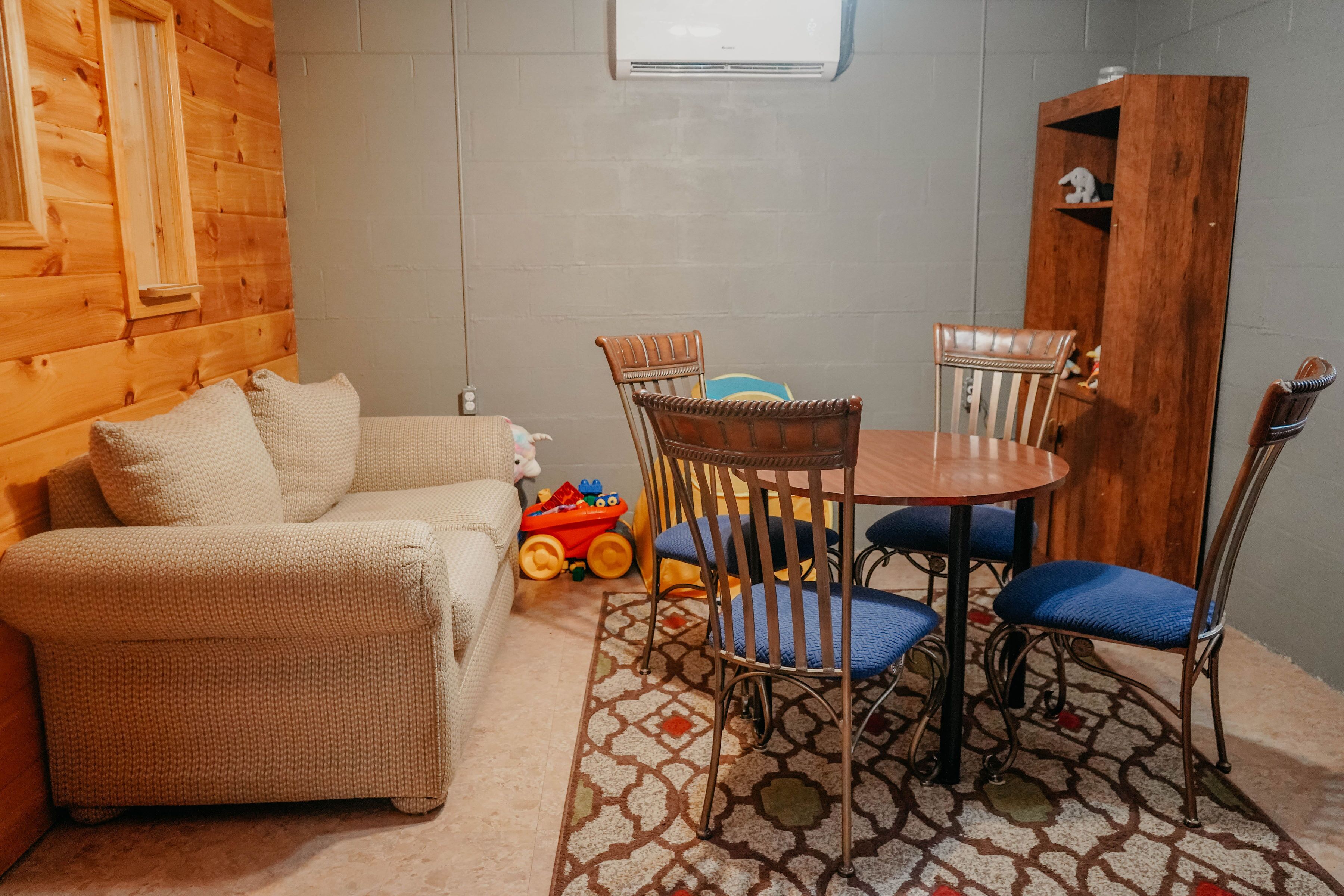 A cozy room with a wooden wall, a sofa, a dining table with chairs, and a patterned rug.