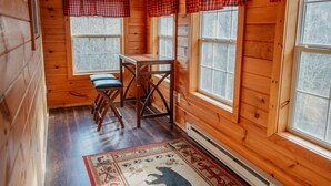 A wooden cabin interior with a dining table and chairs, large windows, and a patterned rug. - Book now to get your free ticket to Dollywood, Anakeesta, and other venues! (Sevierville)