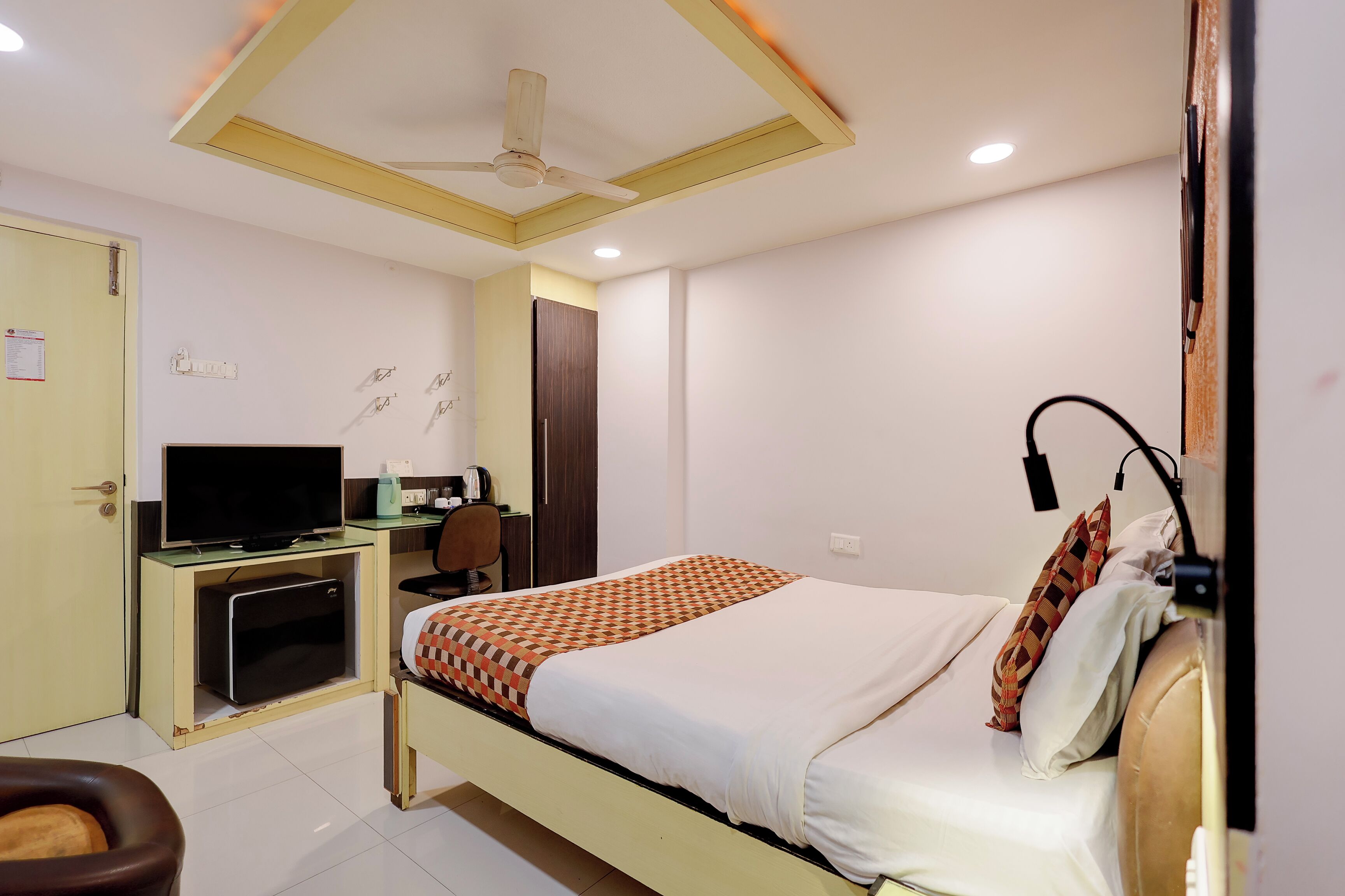 A hotel room with a bed, a desk with a television, a chair, and a ceiling fan.