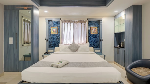 Ein modernes Hotelzimmer mit einem großen Bett, einem Schreibtisch, einem Sessel, einem Kleiderschrank und einem Spiegel.